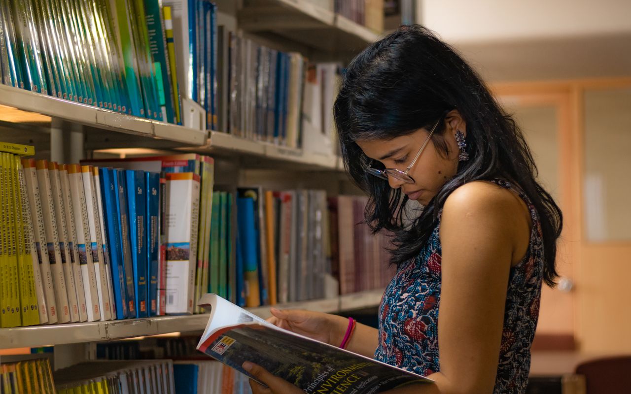 Estudante lendo atentamente um livro em uma biblioteca